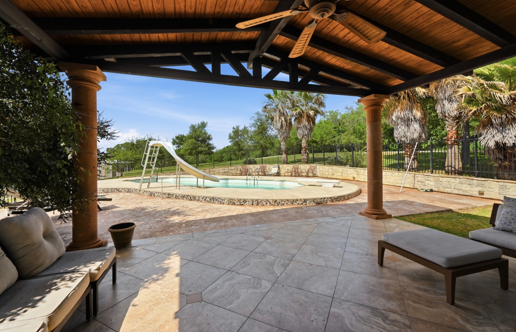1175 Southern Way Luling, TX 78648 - Photo 40 of 40 An inviting outdoor living space features a covered patio with a ceiling fan, overlooking a fenced pool with a slide.