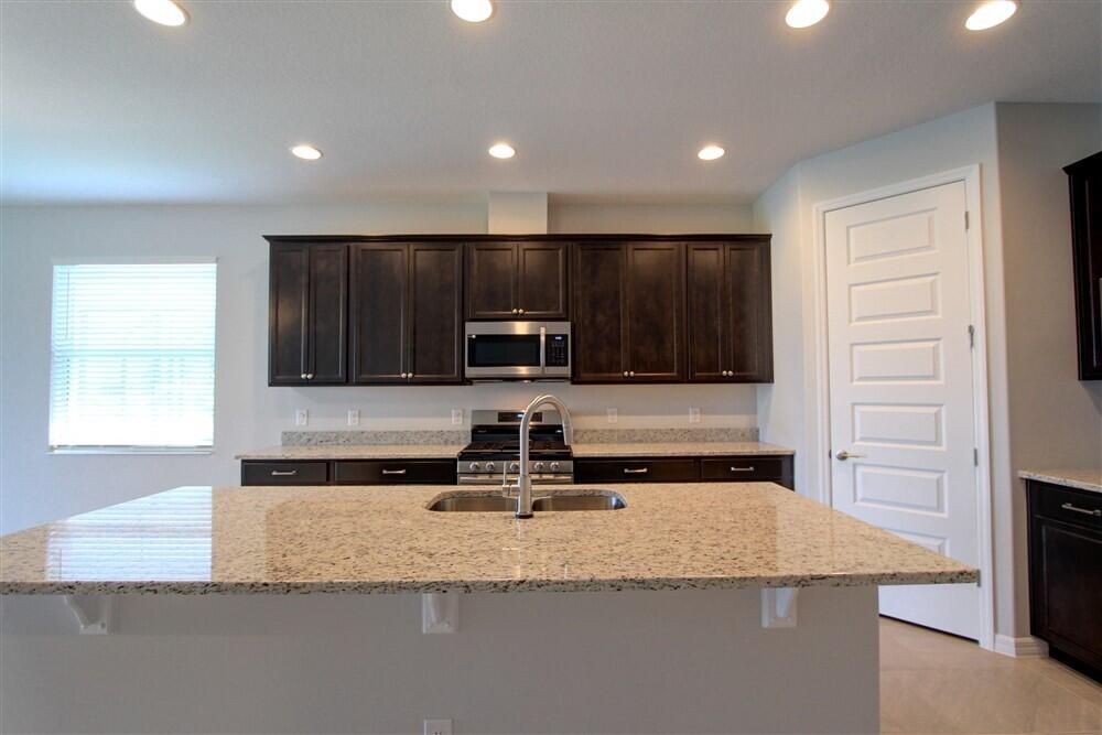 2508 Pangea Circle Melbourne, FL 32940 - Photo 26 of 34 a kitchen with kitchen island granite countertop a stove a sink and a microwave