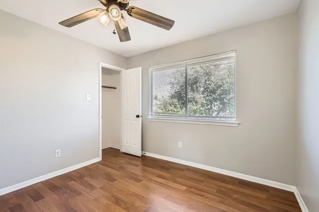 an empty room with wooden floor chandelier fan and windows