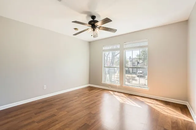 an empty room with wooden floor fan and windows