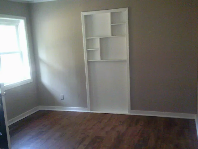 a view of an empty room with wooden floor and a window