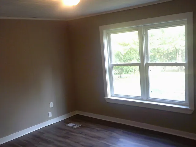 a view of an empty room with wooden floor and a window