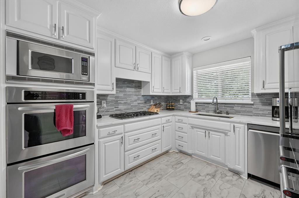 47 Bounty Road East Benbrook, TX 76132 - Photo 7 of 39 Updated kitchen featuring white cabinetry, stainless steel appliances, a gas cooktop, stone-finish countertops, and a gray mosaic tile backsplash