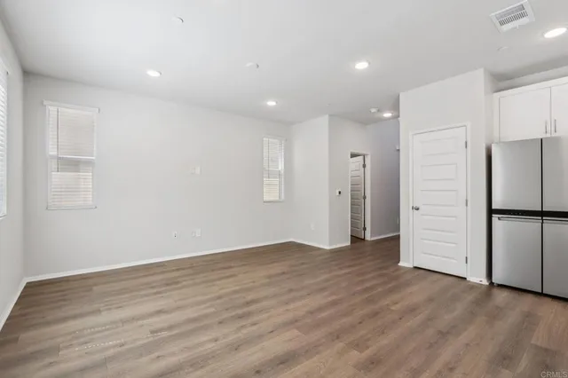a view of an empty room with wooden floor kitchen and a window