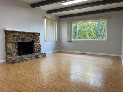 an empty room with wooden floor fireplace and windows
