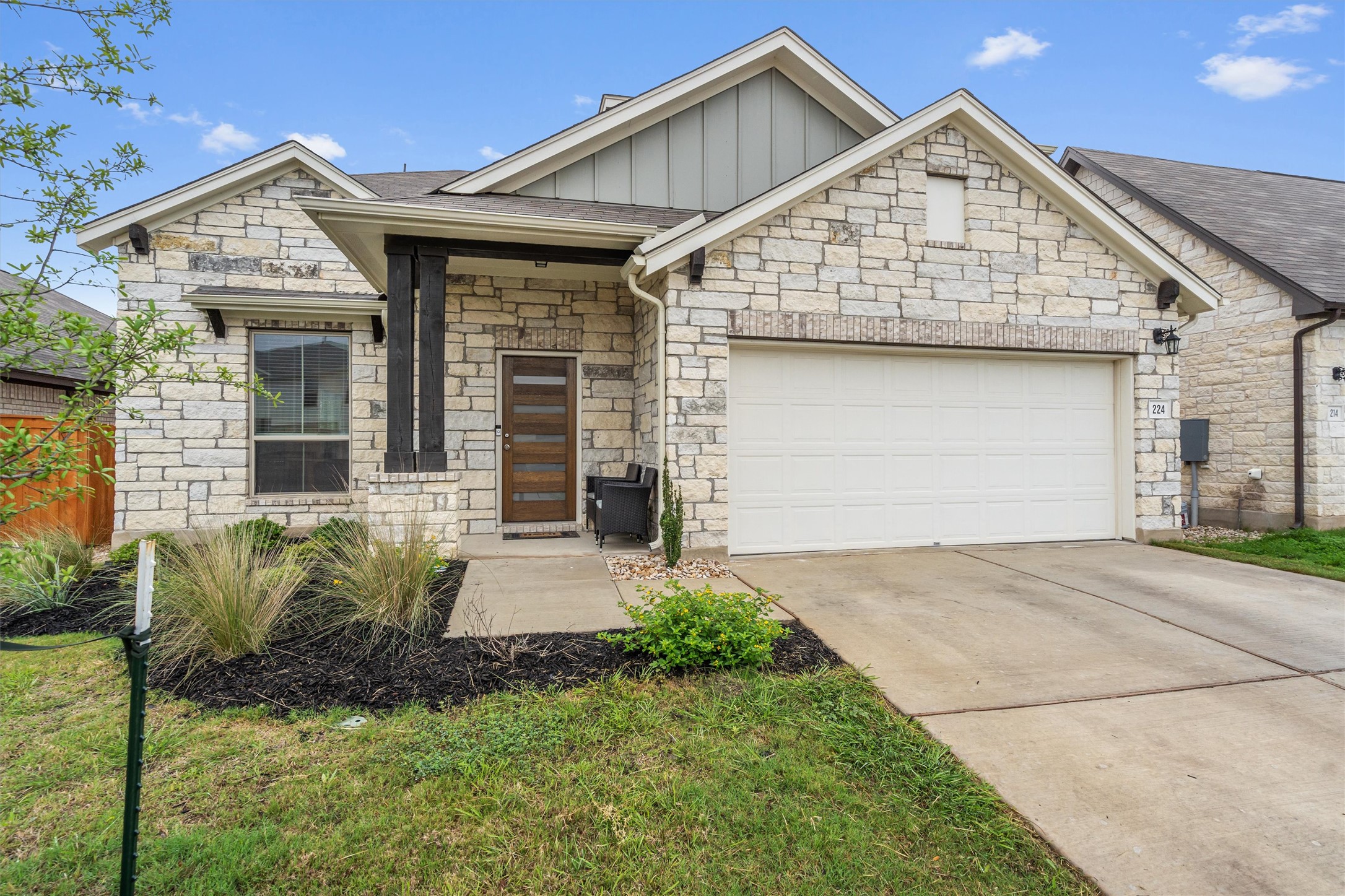 224 Backstays Loop Kyle, TX 78640 - Photo 2 of 19 Stone veneer facade with board and batten siding accents, covered entry featuring dark wood-finish columns, modern front door with horizontal glass inserts, integrated garage, and low-maintenance landscaping