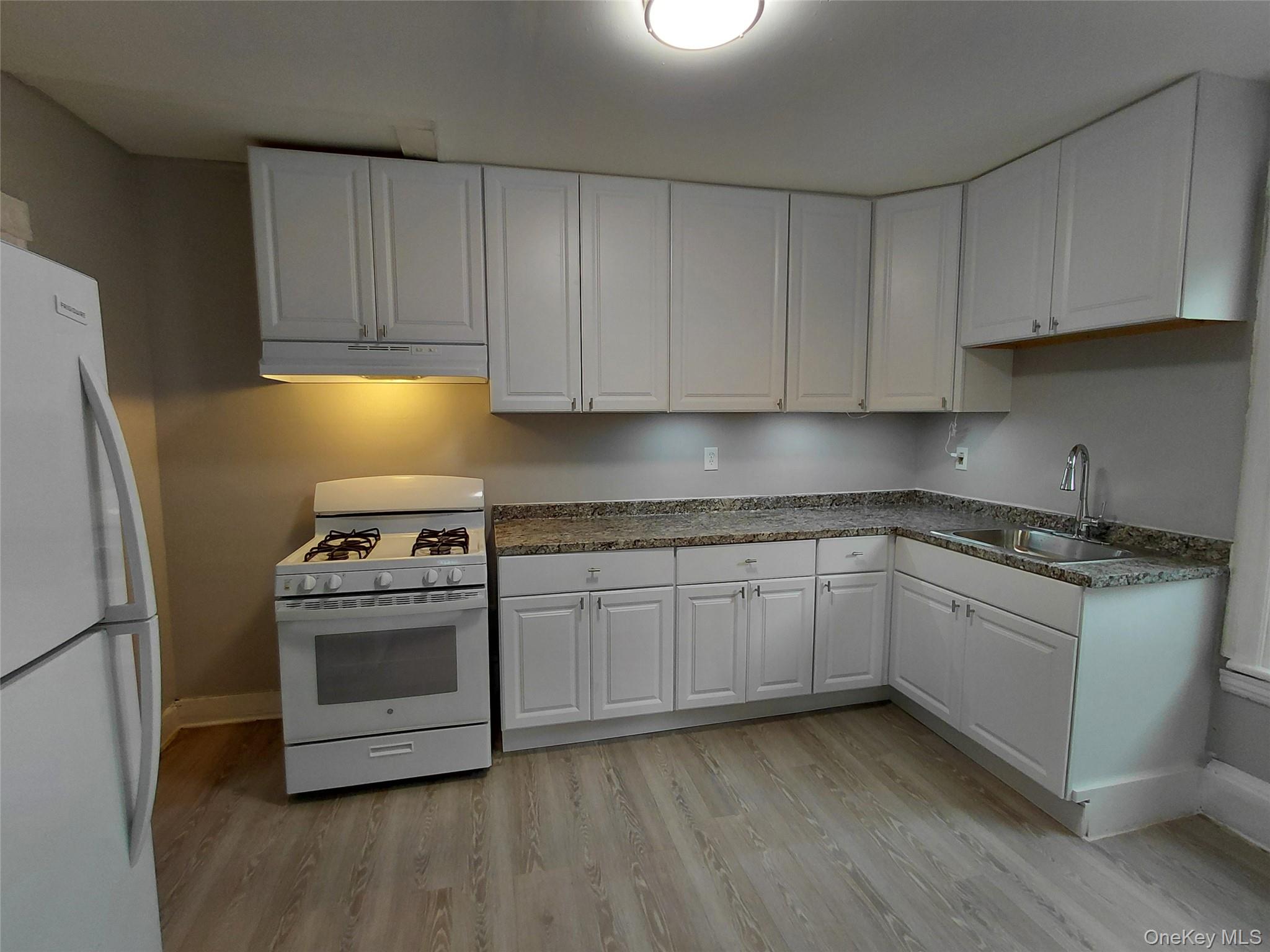 Kitchen with white appliances, white cabinetry, under cabinet range hood, light wood-style flooring, and dark countertops