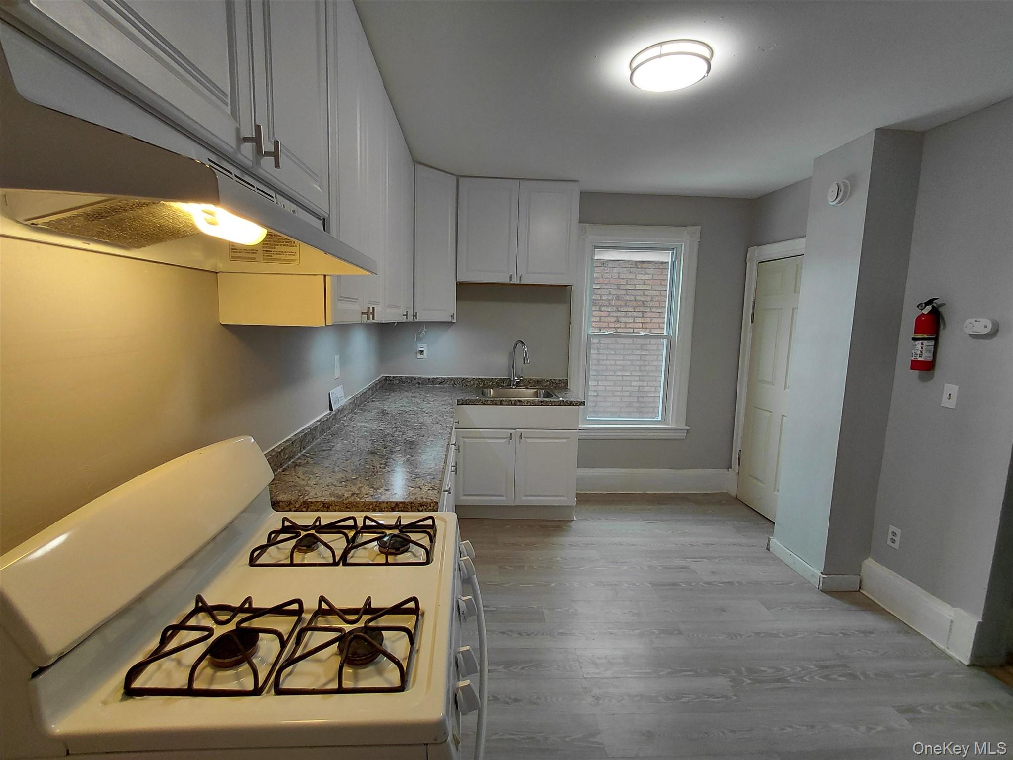 67 Greenkill Avenue, Unit A2 Kingston, NY 12401 - Photo 2 of 13 Kitchen featuring gas range gas stove, white cabinetry, light wood-type flooring, under cabinet range hood, and dark countertops