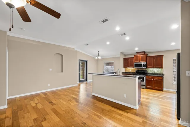 a view of an empty room with wooden floor and a kitchen