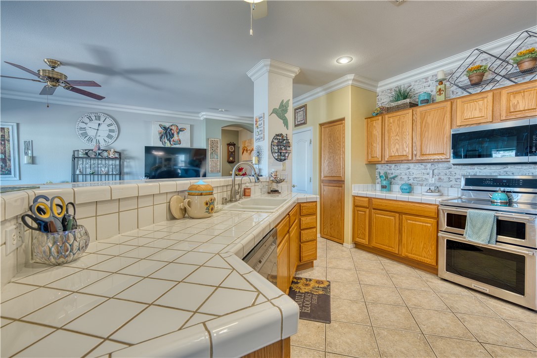 2341 Half Moon Way Bullhead City, AZ 86442 - Photo 19 of 35 Kitchen with tile counters, decorative backsplash, appliances with stainless steel finishes, ornamental molding, and light tile patterned floors