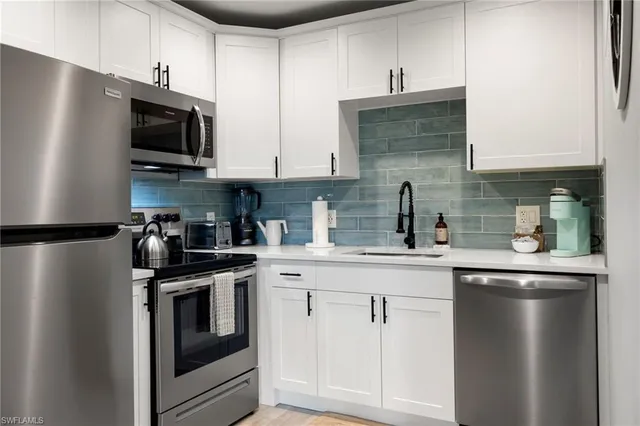 a kitchen with stainless steel appliances granite countertop white cabinets a sink a stove and a refrigerator