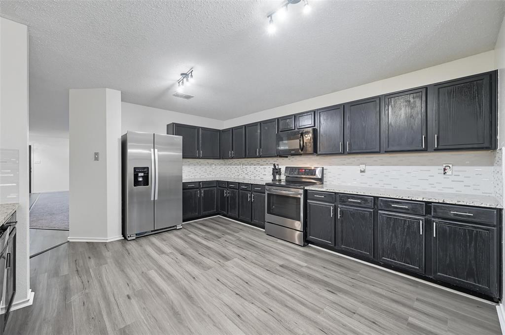1130 Annie Oakley Drive Anna, TX 75409 - Photo 3 of 32 a kitchen with granite countertop wooden floors stainless steel appliances a sink and cabinets