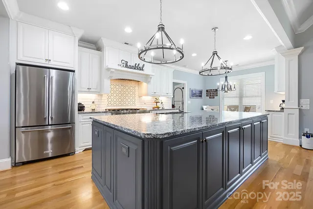 a kitchen with stainless steel appliances granite countertop a refrigerator a sink dishwasher a oven and a dining table with wooden floor