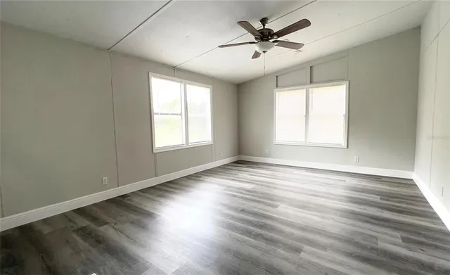 an empty room with wooden floor ceiling fan and windows
