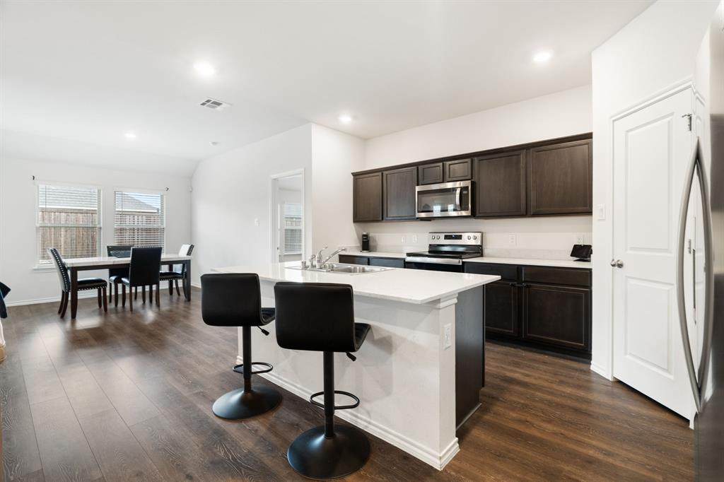 3413 Perman Drive Forney, TX 75126 - Photo 10 of 33 a kitchen with stainless steel appliances granite countertop a refrigerator oven a sink a stove a dining table and chairs with wooden floor