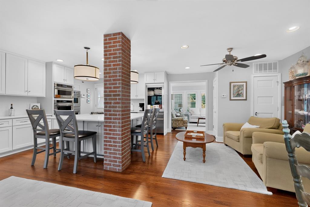 4548 Roland Avenue, Unit A Dallas, TX 75219 - Photo 8 of 31 Kitchen island with seating, white cabinetry, integrated stainless steel appliances, brick column feature, and wood-finish flooring