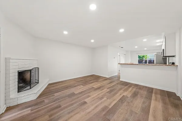 a view of kitchen and empty room with wooden floor and fireplace