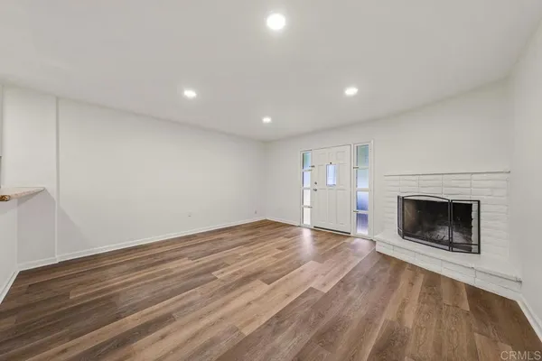 a view of an empty room with wooden floor fireplace and a window