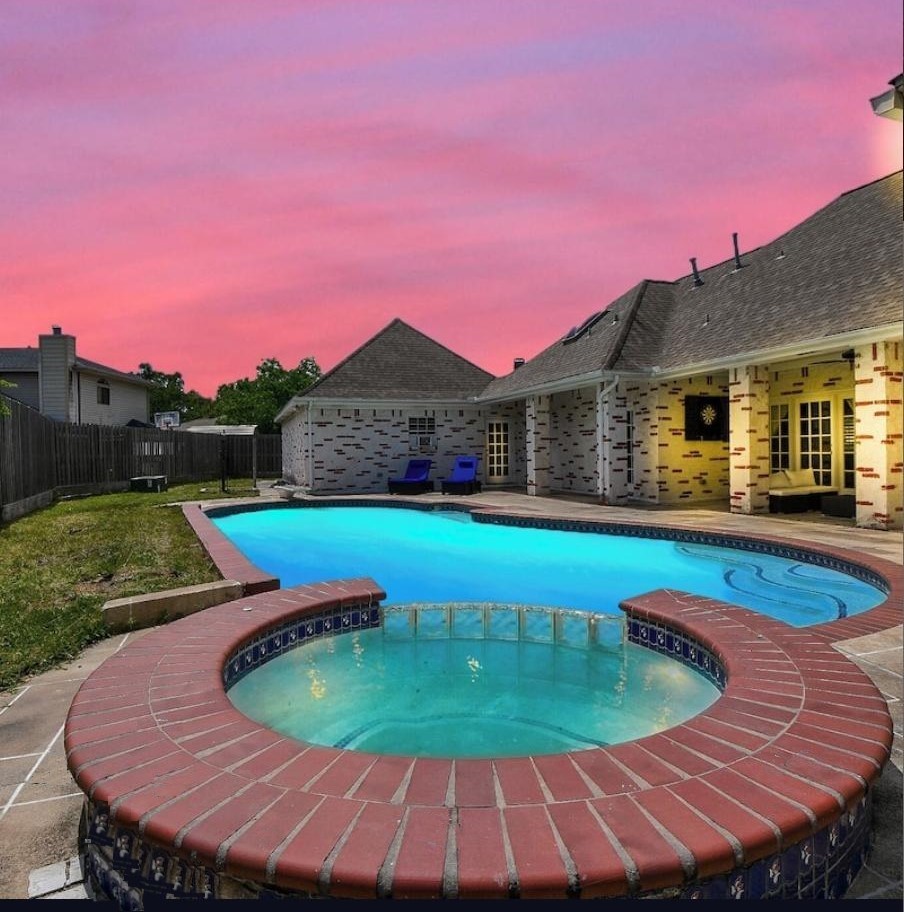 263 Wood Loop Street Houston, TX 77015 - Photo 43 of 45 This photo showcases a backyard with a spacious swimming pool and a hot tub, set against a house with a covered patio area. The sky is a vibrant pink, creating a serene and inviting atmosphere. Perfect for relaxation and entertaining.