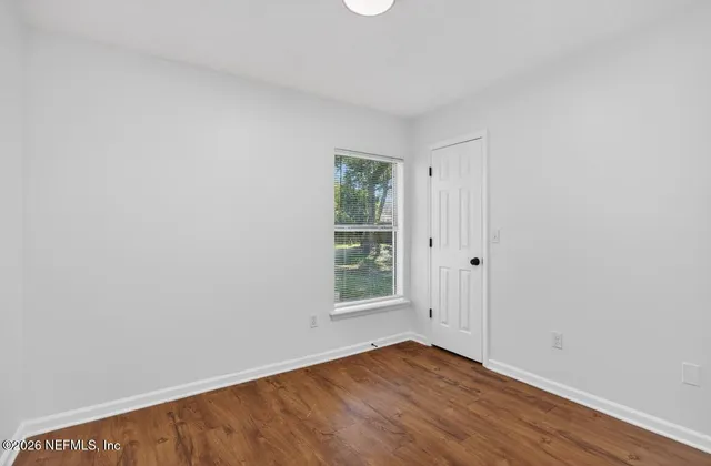 a view of an empty room with wooden floor and a window