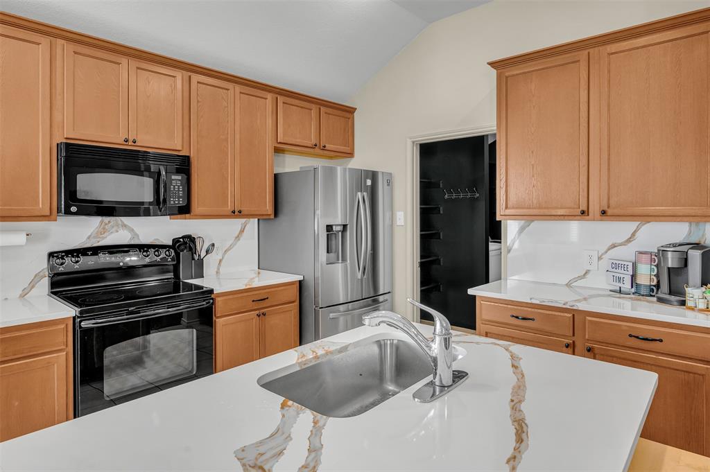 12109 Ridge Tree Road Fort Worth, TX 76036 - Photo 4 of 29 Kitchen with black appliances, light stone counters, and lofted ceiling