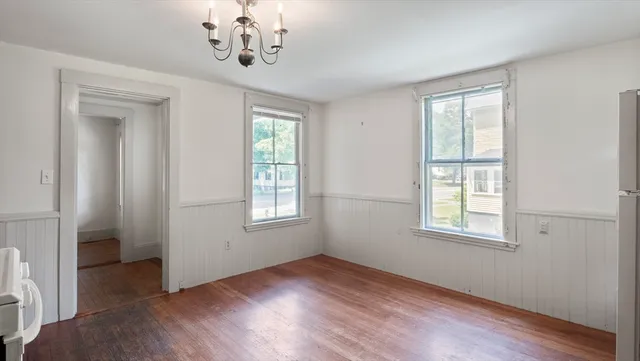 an empty room with wooden floor chandelier and windows
