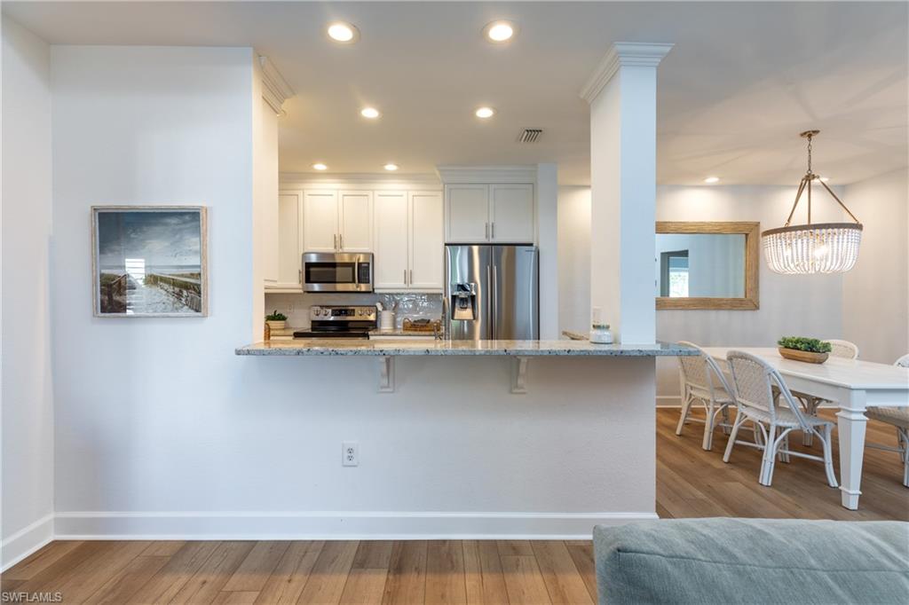 790 Willowbrook Drive, Unit 305 Naples, FL 34108 - Photo 6 of 23 a kitchen with stainless steel appliances granite countertop a stove top oven a sink dishwasher a dining table and chairs with wooden floor