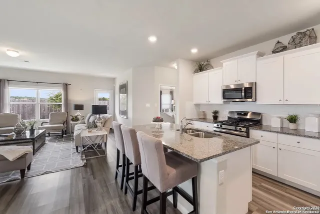 a kitchen with white cabinets a sink stove and chairs with wooden floor