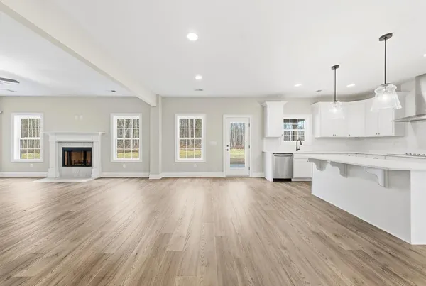 a view of an empty room with wooden floor and kitchen view