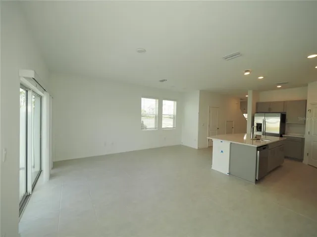 a view of an empty room with kitchen and window