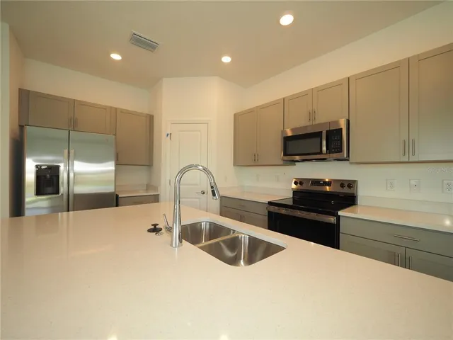a kitchen with stainless steel appliances a sink a stove a microwave a refrigerator a counter top space and cabinets