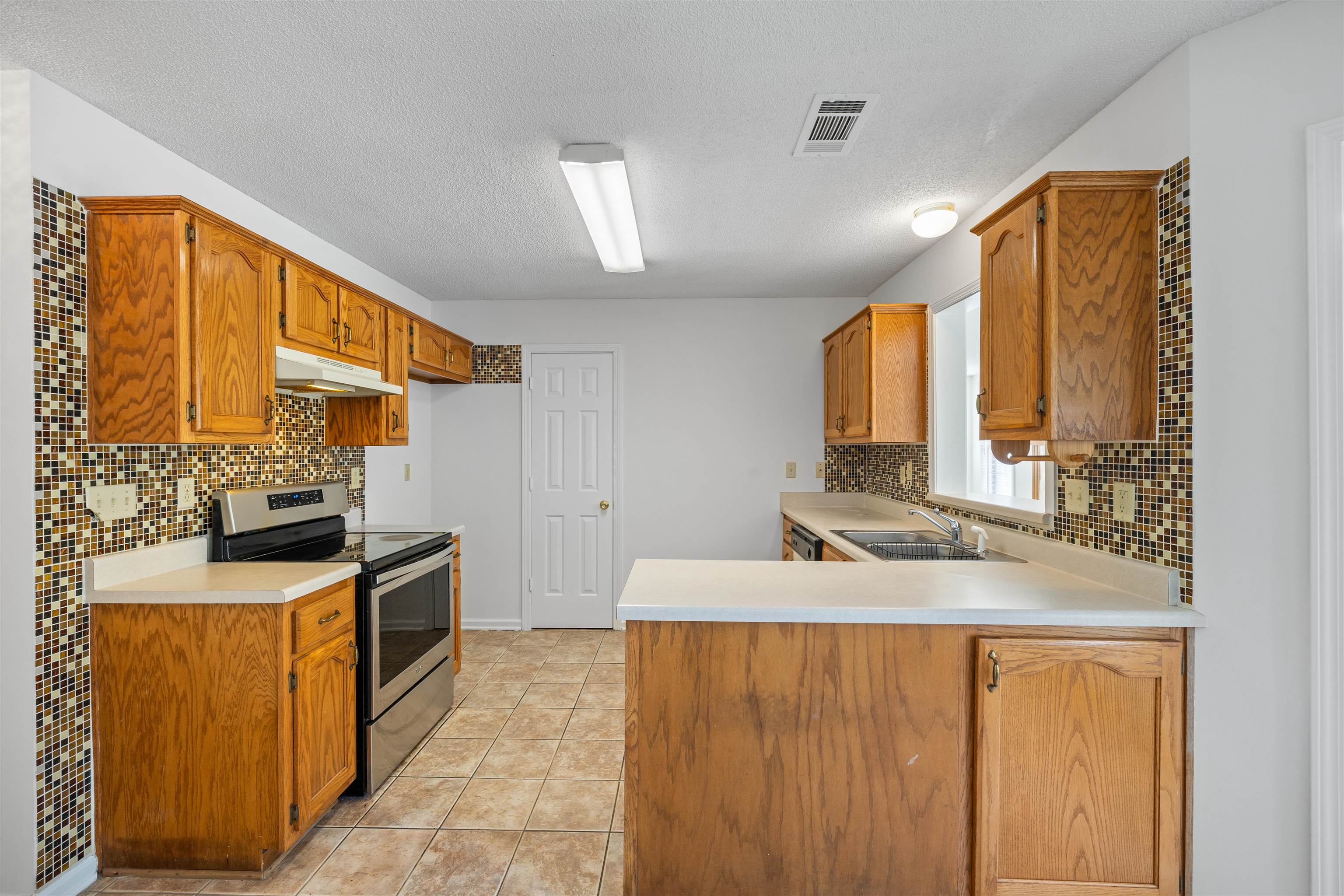 7361 Appling Ridge Drive Cordova, TN 38018 - Photo 16 of 31 Kitchen with electric range, light countertops, a peninsula, light tile patterned floors, and a textured ceiling
