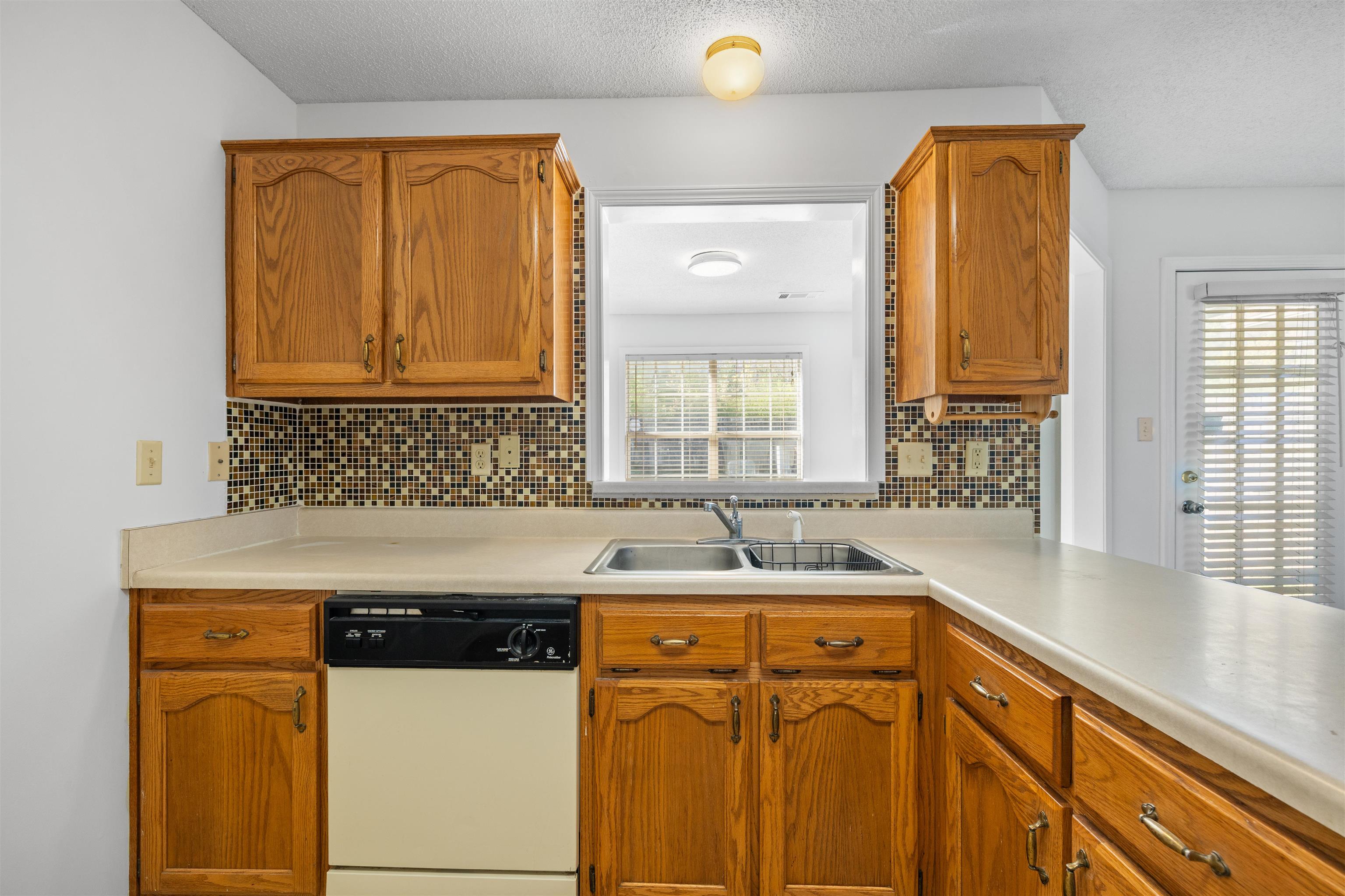 7361 Appling Ridge Drive Cordova, TN 38018 - Photo 17 of 31 Kitchen featuring white dishwasher, light countertops, backsplash, wood finish cabinets, and a textured ceiling