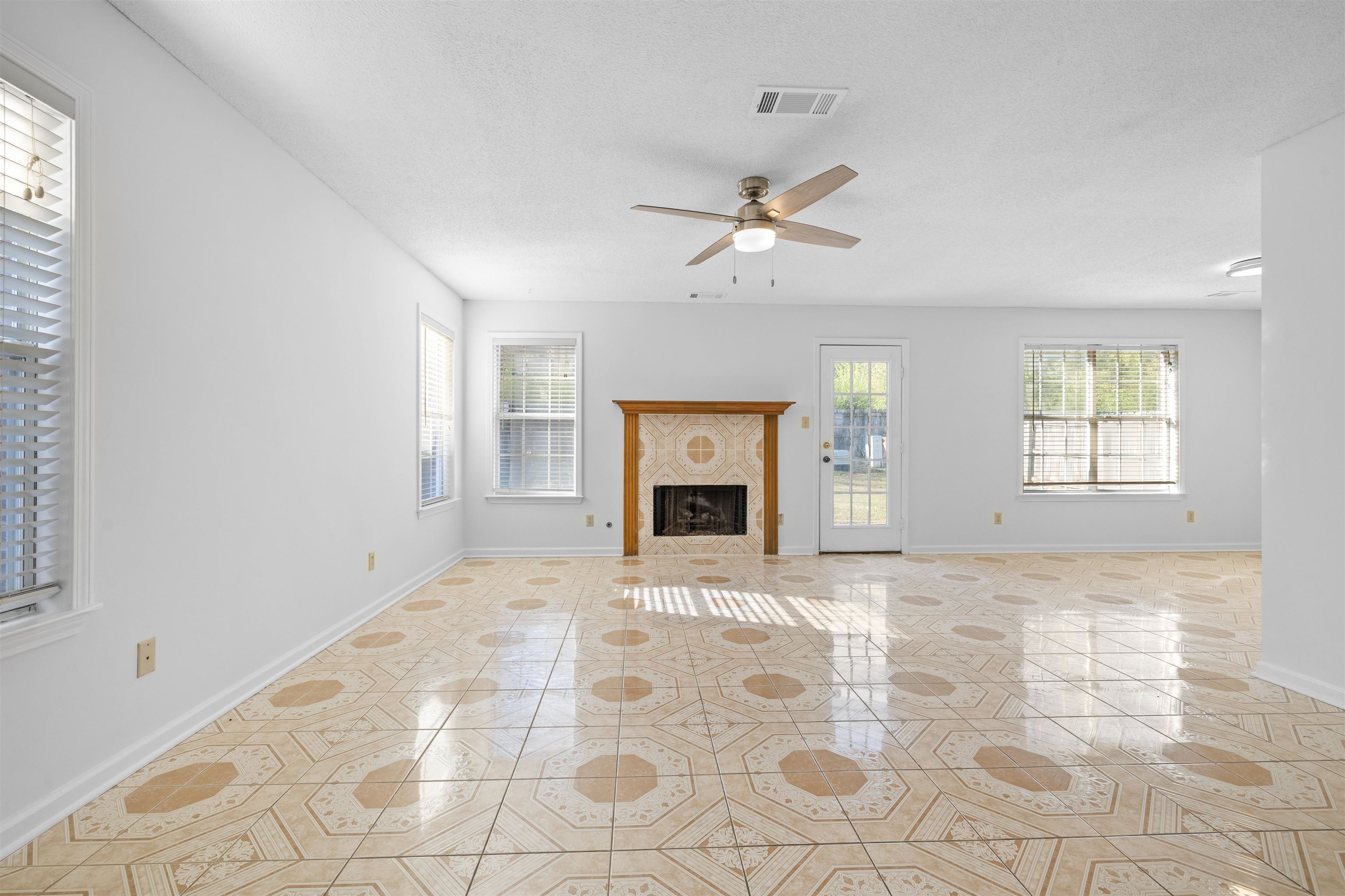 7361 Appling Ridge Drive Cordova, TN 38018 - Photo 4 of 31 Unfurnished living room featuring a tiled fireplace, a ceiling fan, light tile patterned flooring, and a textured ceiling