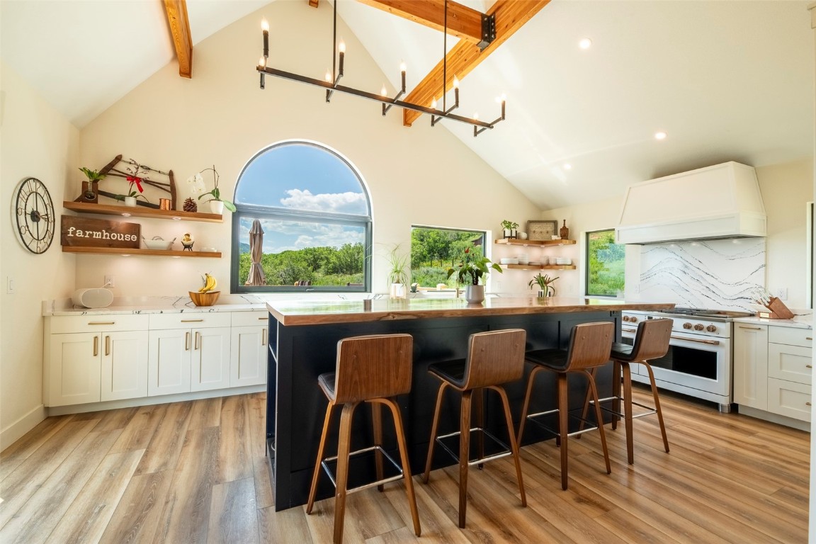 Gourmet kitchen with open shelves, custom range hood, high end white range oven, light wood flooring, and a center island