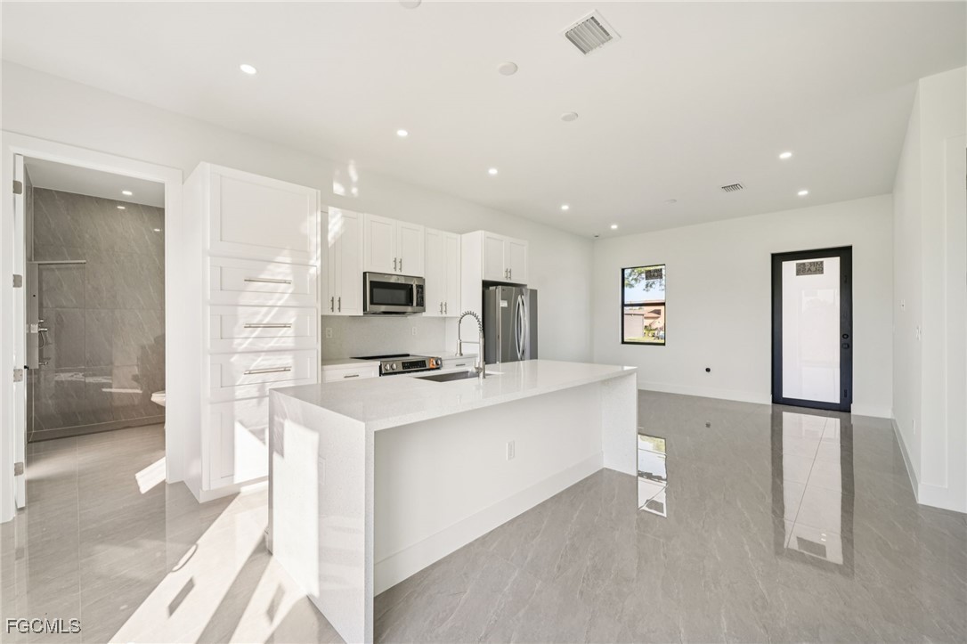 4402 East 19th Street Lehigh Acres, FL 33972 - Photo 15 of 31 a large white kitchen with stainless steel appliances kitchen island a stove a refrigerator a sink dishwasher with a dining table and chairs