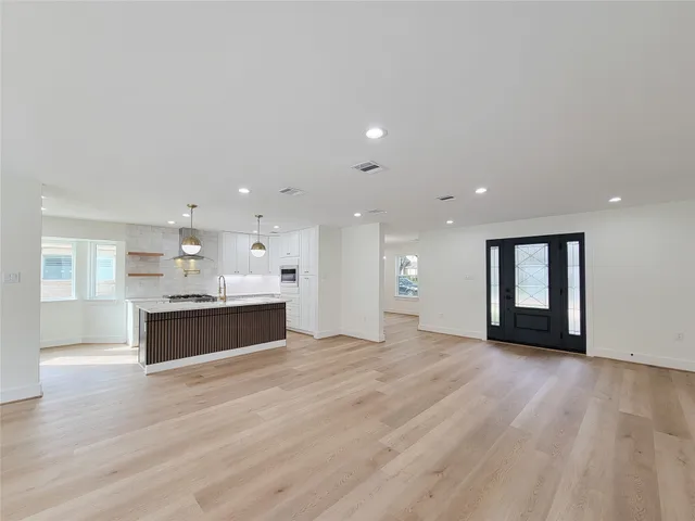 an empty room with wooden floor and kitchen view