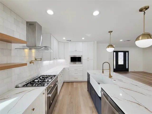 a large kitchen with stainless steel appliances a large counter top a stove and a wooden floors