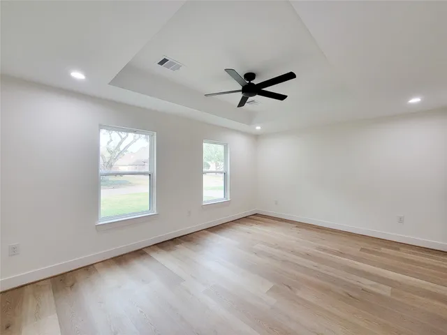 an empty room with wooden floor ceiling fan and windows