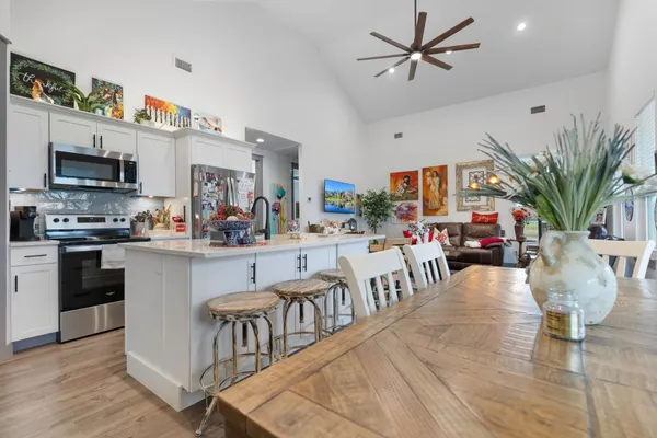 a kitchen with stainless steel appliances granite countertop a refrigerator a stove a sink a dining table and chairs with wooden floor