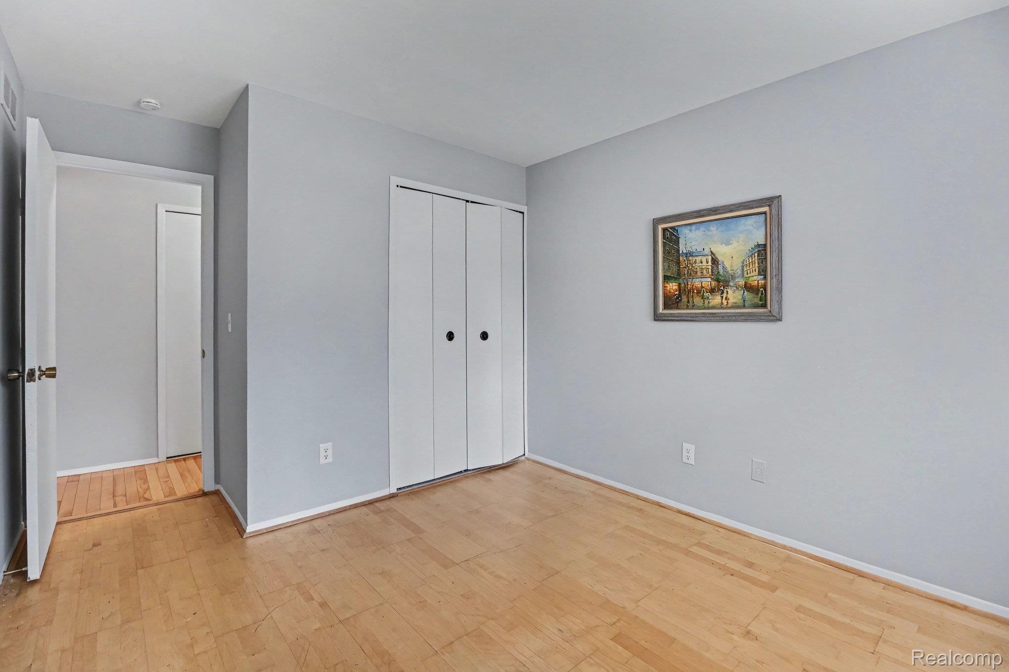29890 West 12 Mile Road, Unit 907 Farmington, MI 48334 - Photo 11 of 18 Room featuring wood-finish flooring, light gray walls, white trim, and bi-fold closet doors