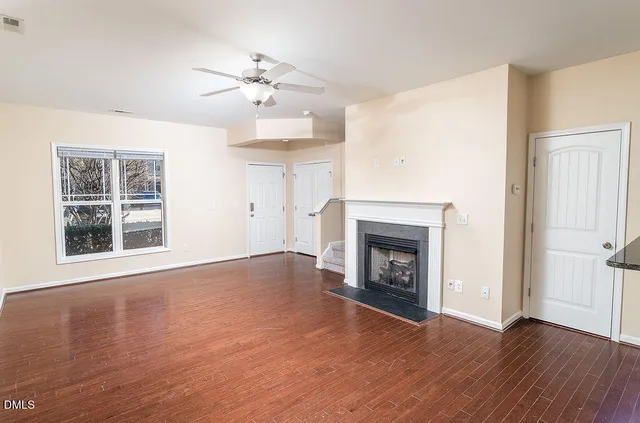 a view of an empty room with wooden floor fireplace and a window