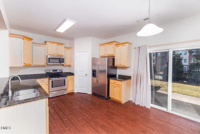 a kitchen with granite countertop wooden floors stainless steel appliances and window