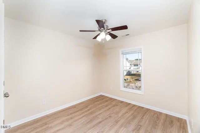 an empty room with wooden floor ceiling fan and windows