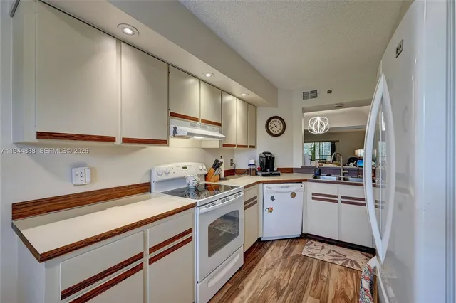 a kitchen with a sink dishwasher a stove and white cabinets with wooden floor