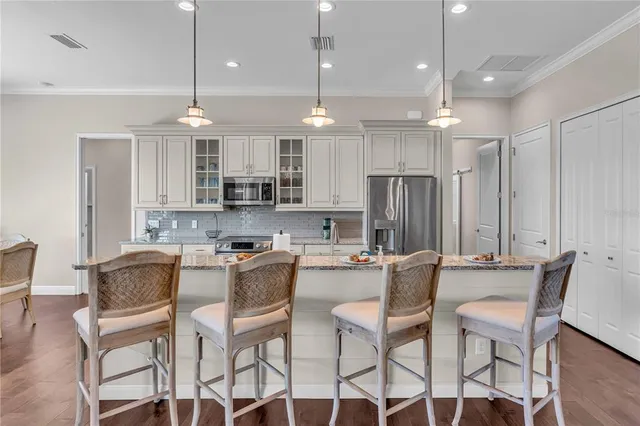 a kitchen with stainless steel appliances kitchen island granite countertop a dining table chairs refrigerator and microwave