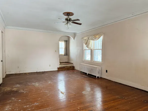 an empty room with wooden floor chandelier fan and windows