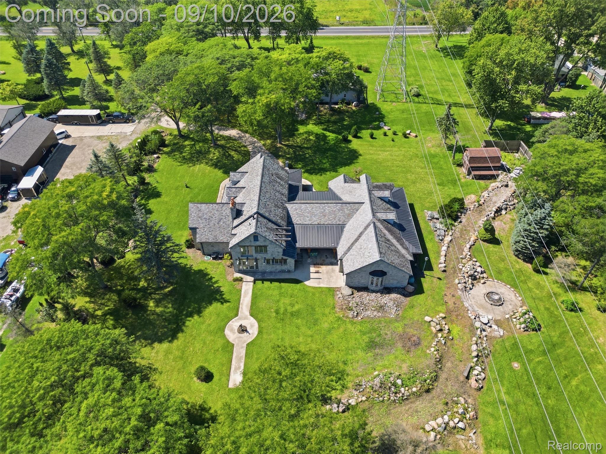 61400 Romeo Plank Road Ray, MI 48096 - Photo 20 of 99 Stone-clad exterior with multiple gables, extensive green lawn, stone-lined landscaping feature, circular stone patio with a fire pit, and mature trees