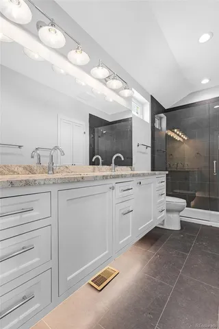a bathroom with a granite countertop sink a toilet a large mirror and shower