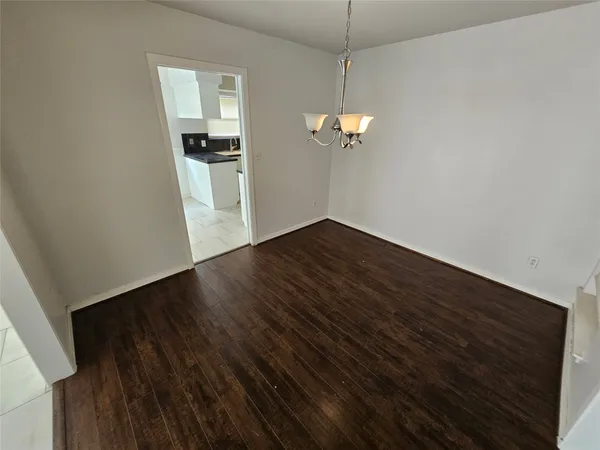 an empty room with wooden floor stairs and a kitchen view